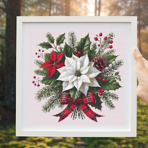 May include: A white poinsettia with red accents, surrounded by green foliage and red berries, tied with a red and green plaid ribbon. The arrangement is framed in a white frame.