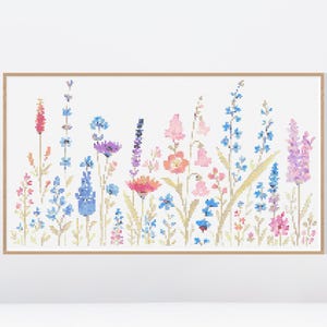 May include: A framed cross-stitch of a wildflower meadow. The artwork features a variety of colorful flowers in shades of pink, blue, purple, and orange, with green stems and leaves. The piece is set against a white background.