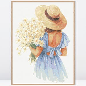 Könnte beinhalten: Ein gerahmter Aquarelldruck einer Person mit Strohhut und hellblauem Kleid, die einen Strauß weißer Gänseblümchen hält. Das Kunstwerk hat eine weiche, pastellfarbene Farbpalette und ein sommerliches Thema.