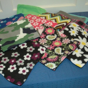 May include: A collection of nine fleece fabric squares with various patterns, including floral, geometric, and camouflage. The squares are arranged in a pile on a blue surface.