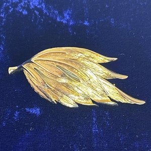 May include: A gold-toned leaf-shaped brooch with a textured surface.