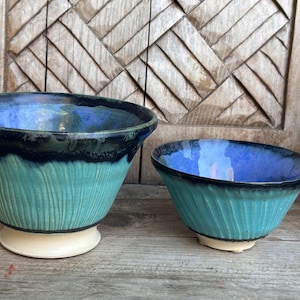 May include: Two ceramic bowls, one larger than the other, with a teal blue glaze and a black rim. The bowls have a textured, wavy design.