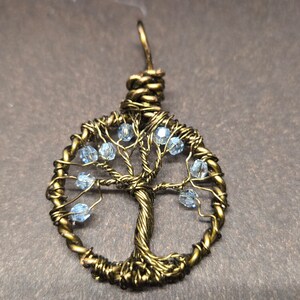 May include: A gold wire wrapped tree of life pendant with light blue crystal beads.