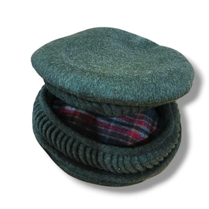 Op de afbeelding: Een donkergroene wollen hoed met een afgeronde bovenkant en een geribbelde, cirkelvormige rand. De binnenvoering heeft een rood, blauw en zwart geruit patroon. Deze hoed is ontworpen voor koud weer.