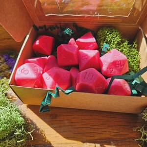 Könnte beinhalten: Eine Schachtel gefüllt mit rosa Würfeln, jeder mit einer anderen Zahl von 1 bis 12. Die Würfel befinden sich in einer braunen Schachtel mit grünem Moos und zerkleinertem Papier.