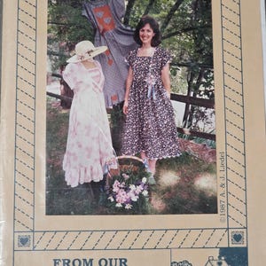 May include: A vintage sewing pattern titled "Garden Dress" from "From Our Calico Cottage." The image shows a woman wearing a floral dress, with two other dresses and a hat displayed. The pattern is from 1987.