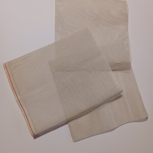 May include: Three pieces of white mesh fabric, folded and stacked on a white surface. The fabric has a fine, even weave and a slightly textured surface.