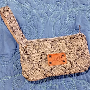 May include: A small, brown snakeskin clutch bag with a zip fastening and a brown leather patch featuring a snake design. The bag has a long, brown leather strap.