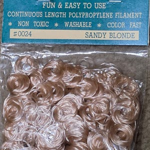 May include: A package of doll hair ringlets in a sandy blonde color. The package has a teal label with the word "RINGLETS" and the text "DOLL HAIR". The package states the hair covers approximately 1 square foot and is fun and easy to use.