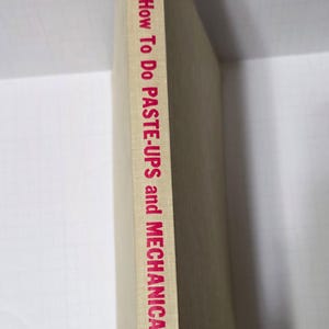 May include: A hardcover book titled "How To Do PASTE-UPS and MECHANICALS" by S. Ralph Maurello. The book's spine is visible, featuring red text on a beige background. The book is a vintage edition.