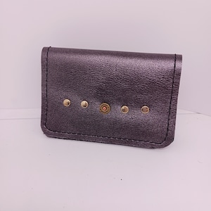 May include: A small, dark purple leather wallet with gold accents and a bullet-shaped charm. The wallet has a flap closure and is decorated with small gold studs.