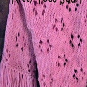 May include: A pink knitted scarf with a lacy pattern and fringe. The scarf has the words "Kitty Toes Scarf" written on it.