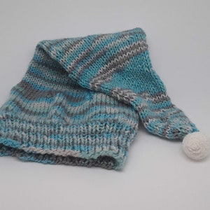 May include: A knitted hat with a long, pointed end and a white pom-pom. The hat features a color pattern of blue, gray, and white stripes. The hat is made of a soft, textured yarn.
