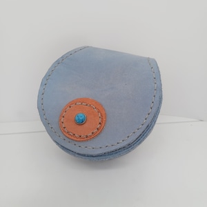 May include: A small, round, light blue leather coin purse with a brown leather circle and a turquoise stone in the centre.