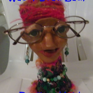 May include: Wacky Bead Lady Eyeglass Holder. A whimsical, handmade eyeglass holder featuring a beaded lady with a pink headband, large glasses, and a colorful beaded necklace.