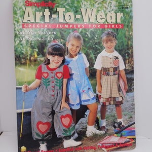 May include: A Simplicity sewing pattern for girls' jumpers. The cover features three girls wearing different styles of jumpers with heart and floral designs. The pattern includes five different designs and instructions for embellishing with quilting, patchwork, and applique. The pattern is for sizes 5-6X.