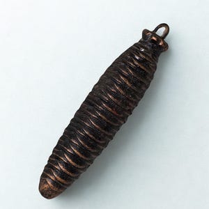 May include: A detailed, bronze-colored pendant shaped like a pine cone. The pendant has a textured surface with ridges and a small loop at the top for hanging. The overall design is naturalistic and detailed.