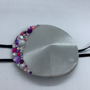 May include: A silver eye patch with a decorative design of pink, purple and white beads.