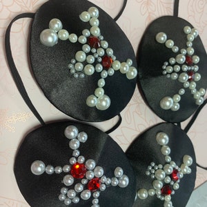 Peut inclure: Quatre patchs oculaires noirs avec un motif d'étoile rouge et blanche. Chaque étoile est faite de perles blanches et d'un strass rouge au centre.