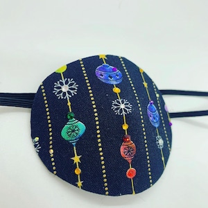 May include: A black eye patch with a Christmas ornament pattern. The ornaments are colorful and have gold glitter accents. The eye patch has an elastic strap.