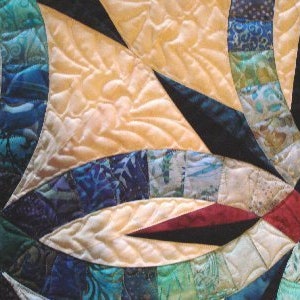 May include: Close-up of a colorful quilt with a complex design. The quilt features a variety of fabrics in shades of blue, green, red, and yellow. The quilting pattern creates a textured effect, with curved and pointed shapes.