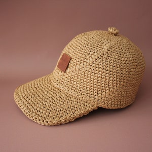 May include: A tan crocheted baseball cap with a brown leather patch on the front.