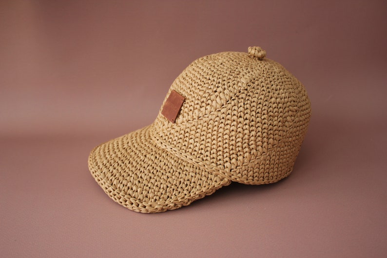 May include: A tan crocheted baseball cap with a brown leather patch on the front.