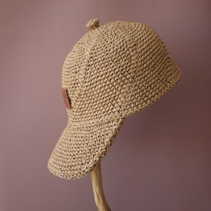 May include: A straw hat with a brown leather patch on the side. The hat is crocheted and has a wide brim.