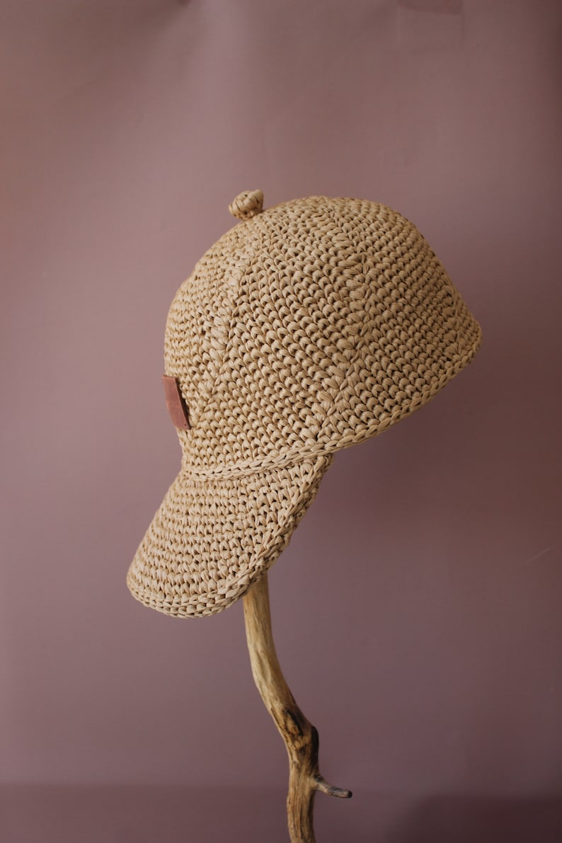May include: A straw hat with a brown leather patch on the side. The hat is crocheted and has a wide brim.