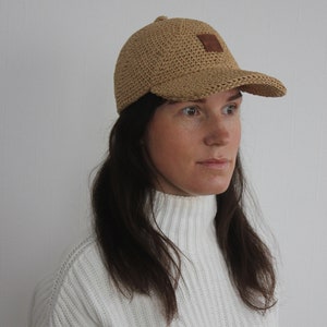 May include: A light brown crocheted baseball cap with a brown leather patch on the front.