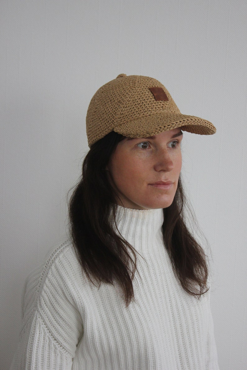 May include: A light brown crocheted baseball cap with a brown leather patch on the front.