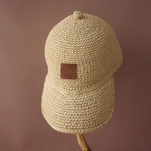 May include: A beige straw baseball cap with a brown leather patch that says "remarkable" on it.