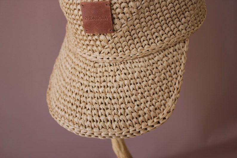 May include: A beige straw hat with a wide brim and a brown leather patch that says "ZHDANOVA".