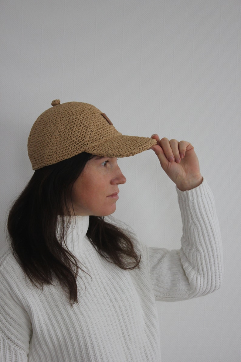 May include: A person wearing a light brown crocheted baseball cap with a brown leather patch on the front.