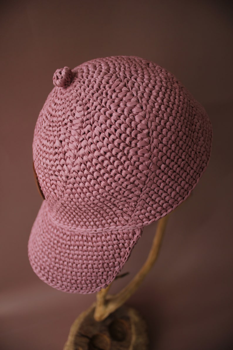May include: A pink crocheted baseball cap with a curved brim. The cap is made of a soft, textured yarn and has a simple, classic design.