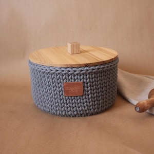 May include: Gray knitted storage container with a wooden lid and a leather label that says "ZOHARAKOV HOME".