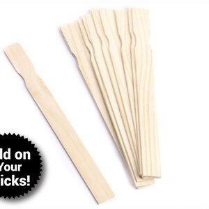 May include: A bundle of 10 wooden craft sticks, each approximately 6 inches long, with a rounded end and a flat, slightly wider end. The sticks are arranged in a fan shape, with the rounded ends facing outward. The sticks are a natural wood color.
