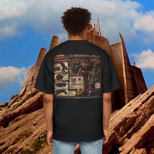 May include: Black t-shirt featuring a detailed graphic on the back with Japanese text and illustrations of robots and charts. The shirt is worn by a person with curly hair, set against a backdrop of a mountain and blue sky.
