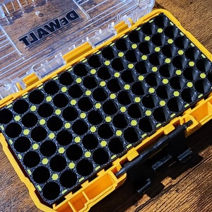 May include: An open yellow and black plastic storage case with the word "DEWALT" printed on the lid. The case has a grid of 48 small, round, black compartments with yellow dots.
