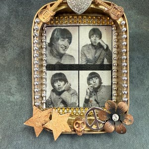 May include: A gold-toned metal tin with a collage of four black and white photos of the Beatles. The tin is decorated with a peace sign, a skull, two gold stars, a flower with a rhinestone, and a rhinestone heart.