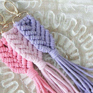 May include: Three handmade macrame keychains with gold key rings. The keychains are made with ombre yarn in shades of pink and purple.