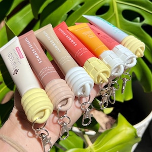 May include: Six colourful lip balm tubes with keychains. The tubes are labelled "Summer Fridays" and "Butter Balm".
