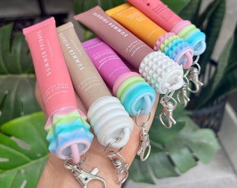 Puede incluir: Seis tubos de bálsamo labial coloridos con llaveros. Los tubos son de color rosa, naranja y rosa claro con el texto "SUMMER FRIDAYS" y "LIP BUTTER BALM" impreso en ellos. Los llaveros están hechos de silicona de colores y tienen diferentes formas.