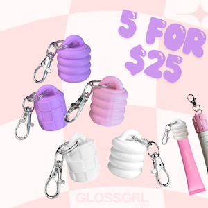 May include: Five colourful silicone lip gloss keychain caps in purple, pink and white. The caps are designed to fit over lip gloss tubes. The text "5 FOR $25" is in the top right corner of the image. The text "GLOSSGIRL caps" is in the bottom left corner of the image.