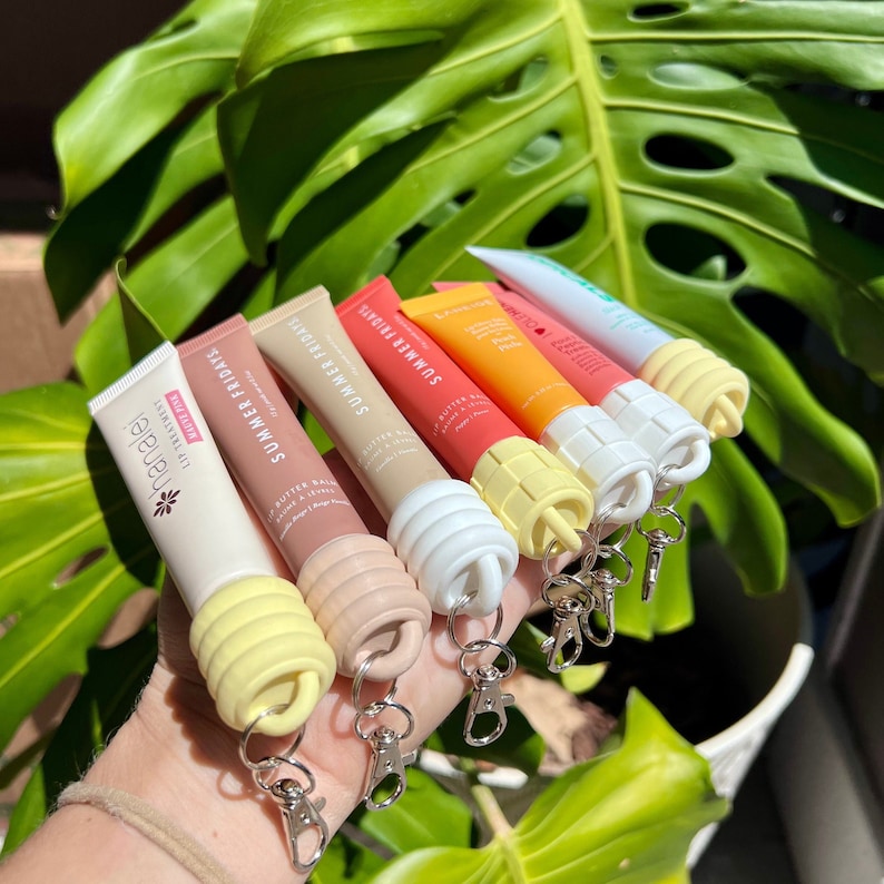 May include: Six colourful lip balm tubes with keychains. The tubes are labelled "Summer Fridays" and "Butter Balm".