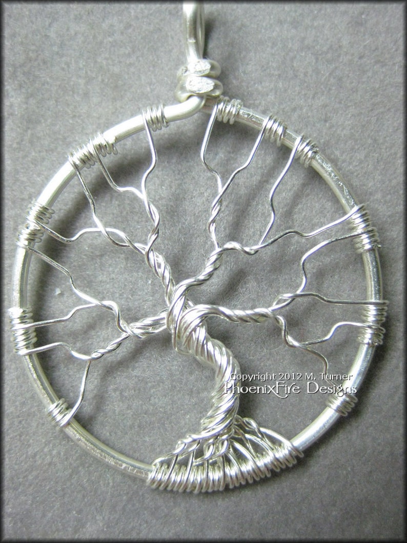 May include: A silver wire tree of life pendant with a circular frame and a twisted wire trunk. The pendant is made of wire and has a delicate, intricate design. Copyright 2012 M. Turner PhoenixFire Designs.