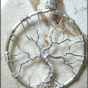 May include: A silver wire tree of life pendant with a circular design. The pendant is made of wire that is twisted and shaped to resemble a tree with branches and leaves. The pendant is on a white background.