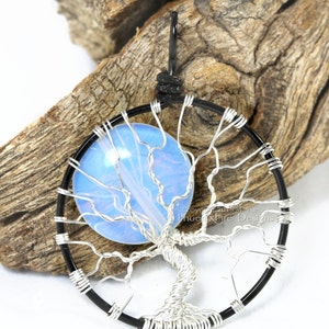 May include: A silver wire wrapped tree of life pendant with a blue opal stone in the centre. The pendant is hanging from a black cord.