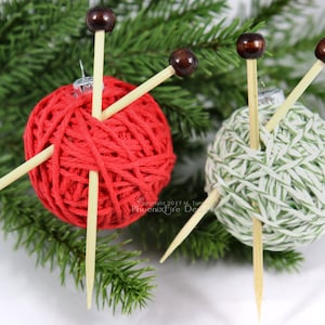 Puede incluir: Dos ovillos de lana envueltos en hilo rojo y verde con agujas de tejer de madera que sobresalen. Los ovillos de lana son adornos para un &aacute;rbol de Navidad.