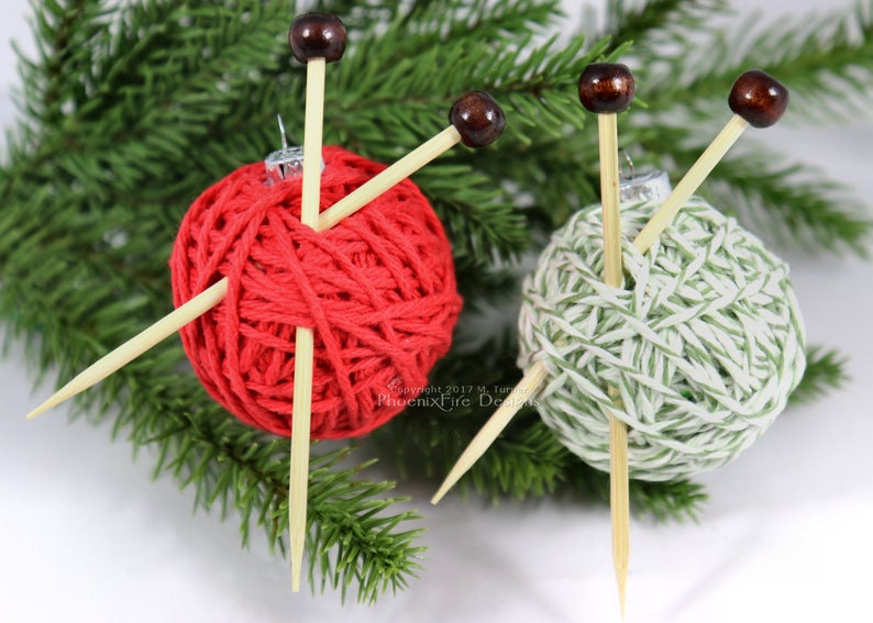 Puede incluir: Dos ovillos de lana envueltos en hilo rojo y verde con agujas de tejer de madera que sobresalen. Los ovillos de lana son adornos para un &aacute;rbol de Navidad.